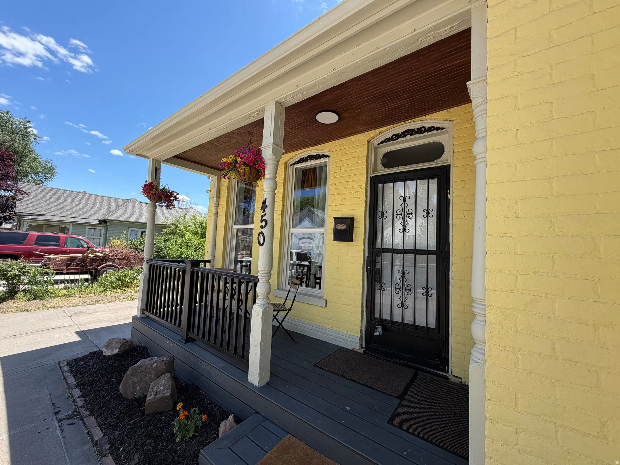 Inviting front porch featuring a dark wood-finish deck, white columns, black railing, and a decorative security screen door