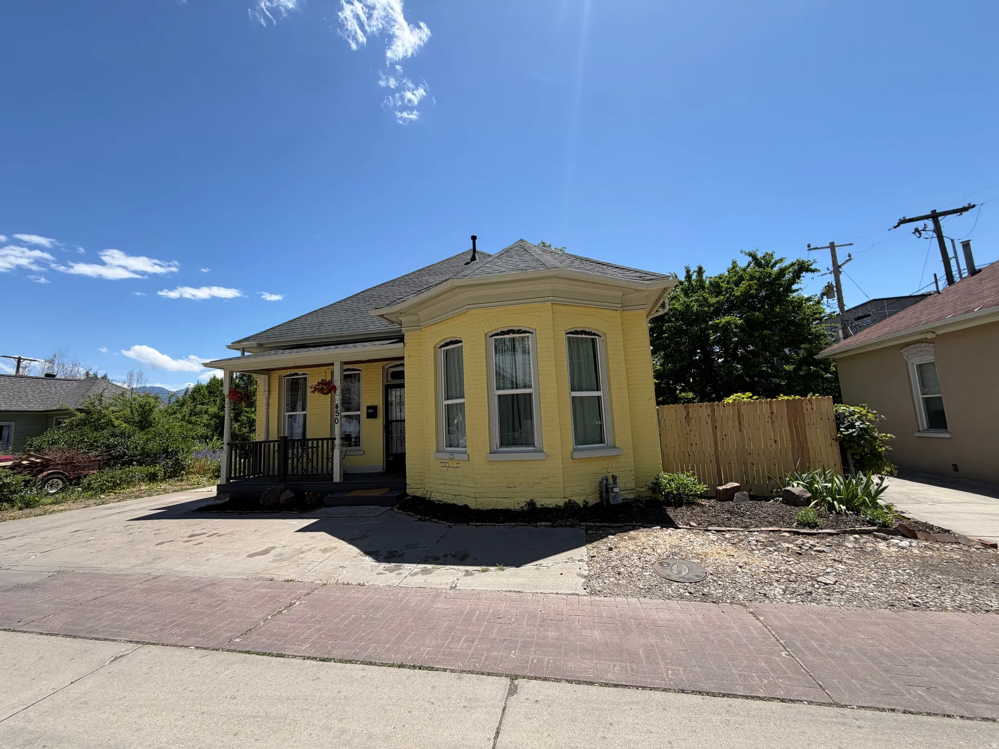 Yellow exterior featuring a prominent bay window with multiple vertical windows, a covered front porch, dark porch railing, and a gabled roof