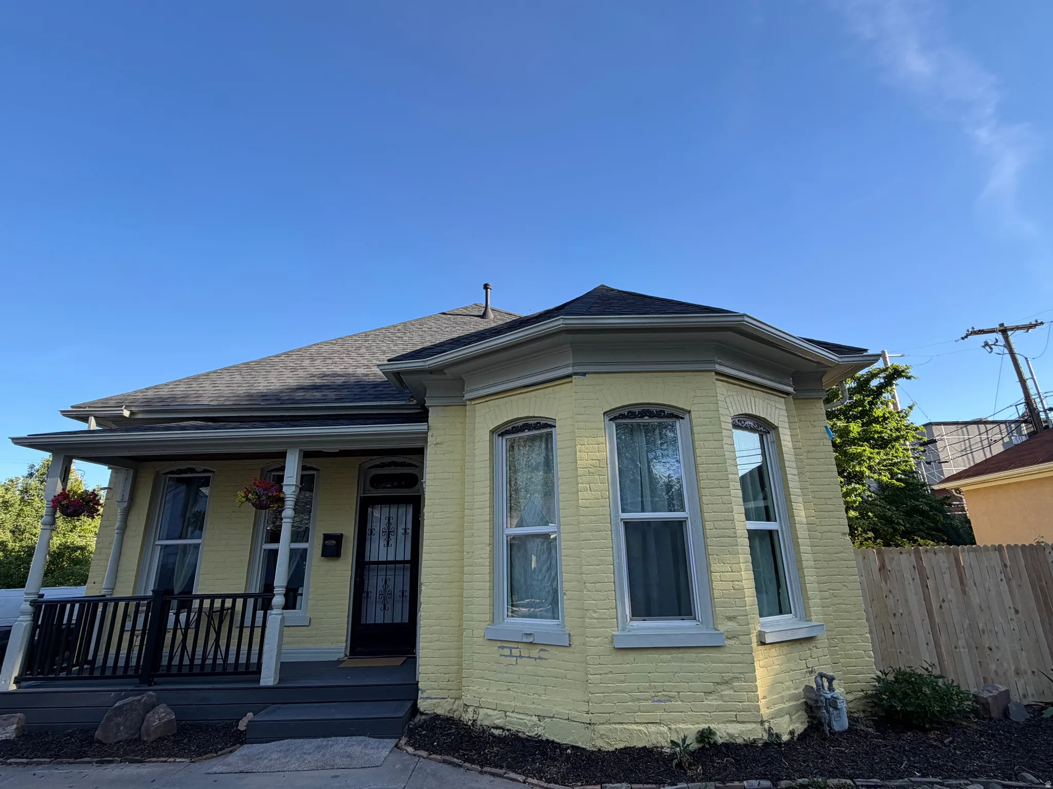 Yellow brick exterior with a prominent bay window, covered front porch, dark-stained wood railings, and a newly installed wood privacy fence