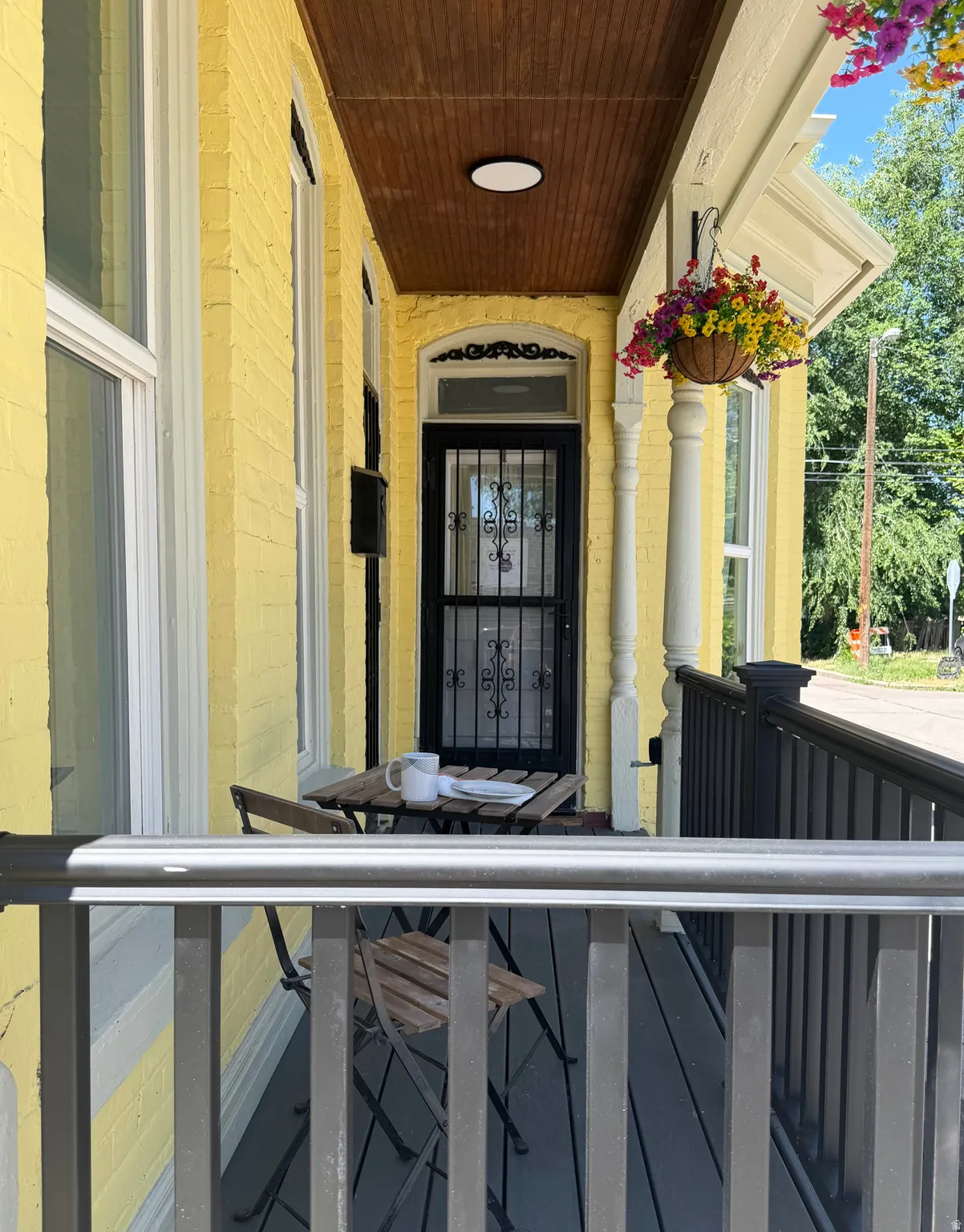 Covered front porch featuring a wood-finish ceiling, yellow painted brick exterior, and a black wrought iron security door