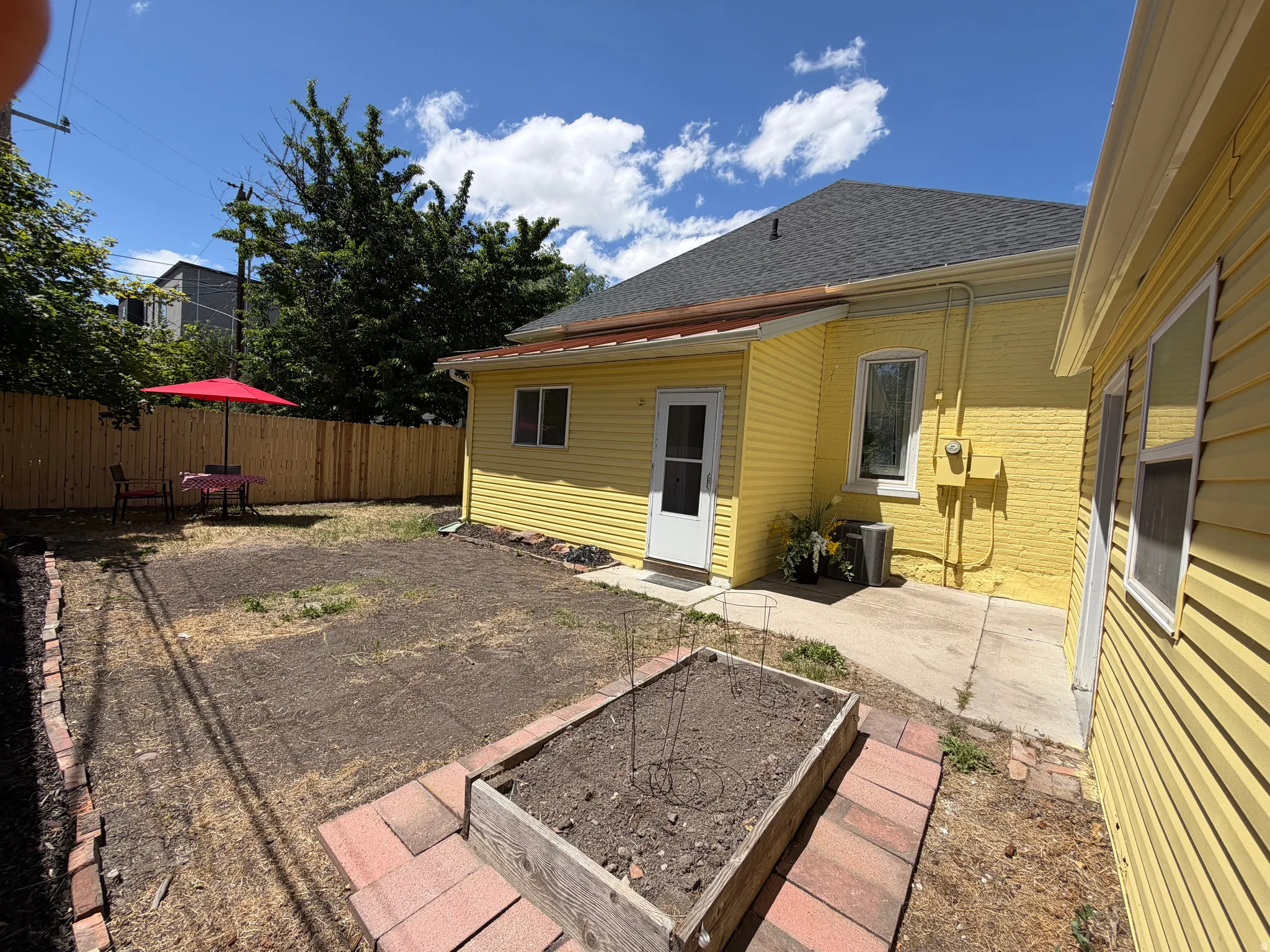Spacious backyard featuring a wood privacy fence, concrete patio, a raised garden bed with brick trim, and direct exterior access