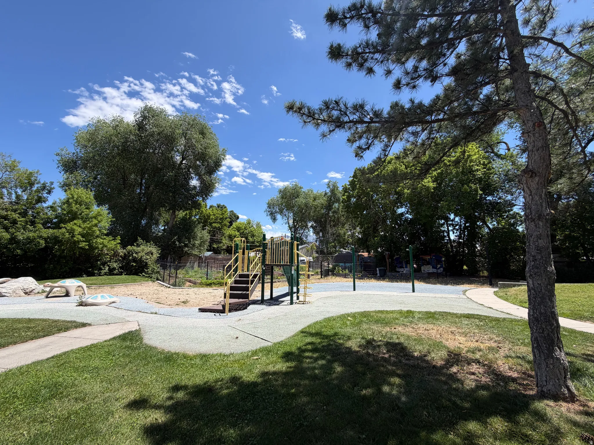Expansive outdoor area featuring a playground with stairs and slides, surrounding sand and soft-surface ground, and a paved pathway