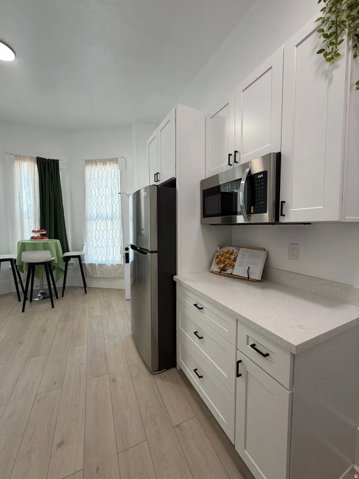 Contemporary kitchen featuring white shaker cabinetry, stainless steel appliances, light-toned wood-finish flooring, and speckled light countertops