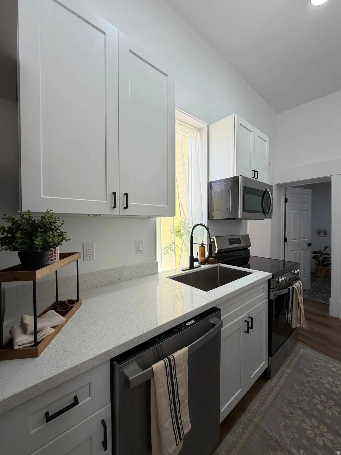 Contemporary kitchen featuring white shaker cabinetry with matte black hardware, a stainless steel sink with a black faucet, and light-toned solid surface countertops