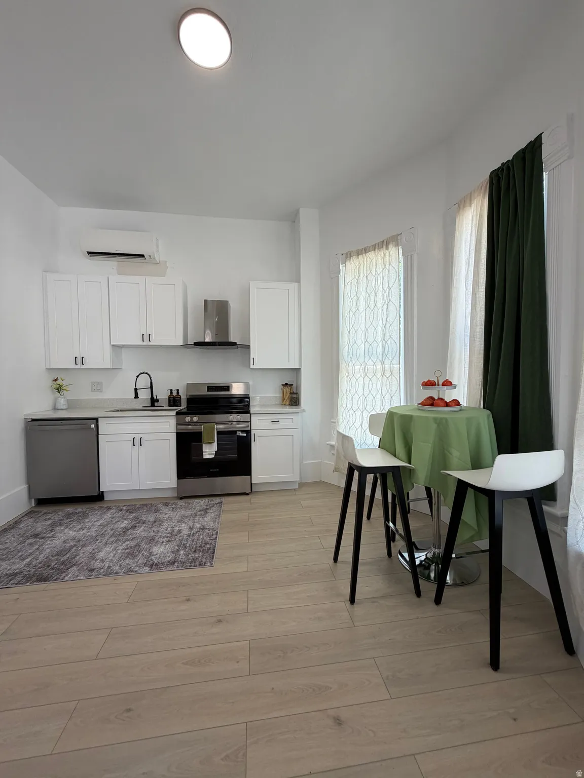 Contemporary kitchen featuring white cabinetry, stainless steel appliances, light wood-finish flooring, and solid surface countertops