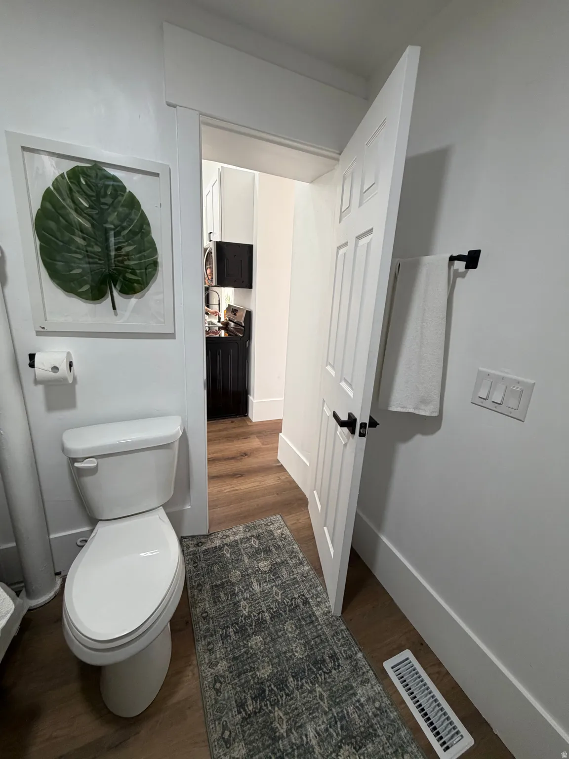 Powder room featuring wood-finish flooring, white paneled door with black hardware, and a white toilet