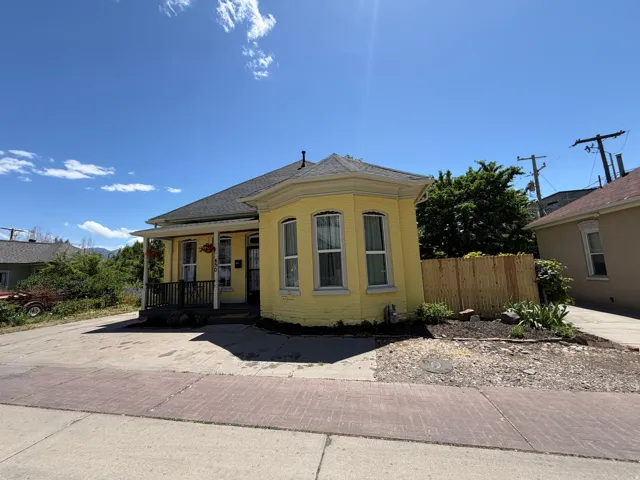 Yellow exterior featuring a prominent bay window with multiple vertical windows, a covered front porch, dark porch railing, and a gabled roof
