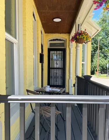 Covered front porch featuring a wood-finish ceiling, yellow painted brick exterior, and a black wrought iron security door