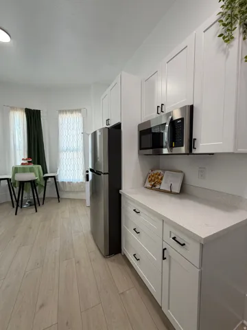 Contemporary kitchen featuring white shaker cabinetry, stainless steel appliances, light-toned wood-finish flooring, and speckled light countertops