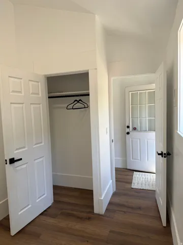 Interior space featuring wood-finish flooring, white paneled doors, and a built-in closet with hanging rod