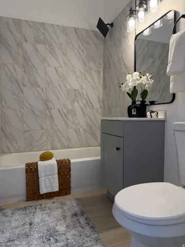 Full bathroom featuring a tub with a rain shower head, large-format marble-look wall tiling, a contemporary vanity with a white countertop, and wood-finish flooring