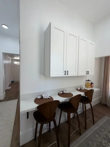 Built-in kitchen bar featuring a light-toned countertop, white cabinetry with dark hardware, and wood-finish flooring
