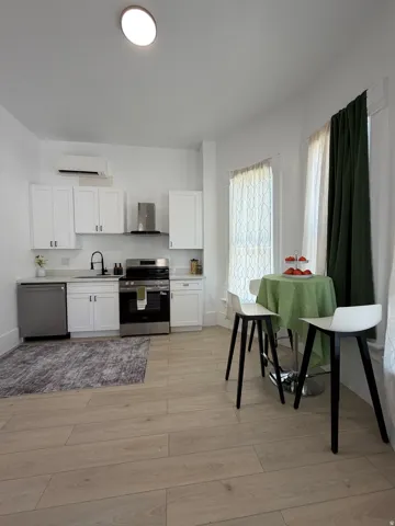 Contemporary kitchen featuring white cabinetry, stainless steel appliances, light wood-finish flooring, and solid surface countertops