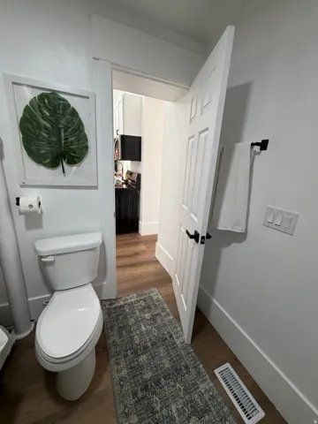 Powder room featuring wood-finish flooring, white paneled door with black hardware, and a white toilet