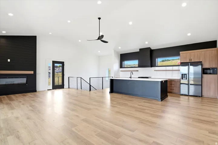 Open-concept living space featuring wood-finish flooring, a modern black shiplap fireplace surround with a light wood mantel, and vaulted ceilings with recessed lighting