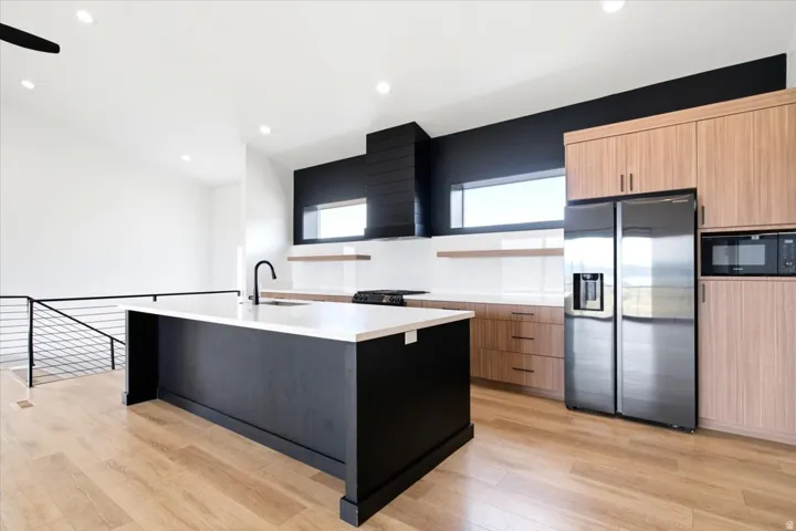 Kitchen featuring a large central island with a white countertop and black base, wood-finish flooring, two-tone cabinetry, stainless steel appliances, and horizontal windows