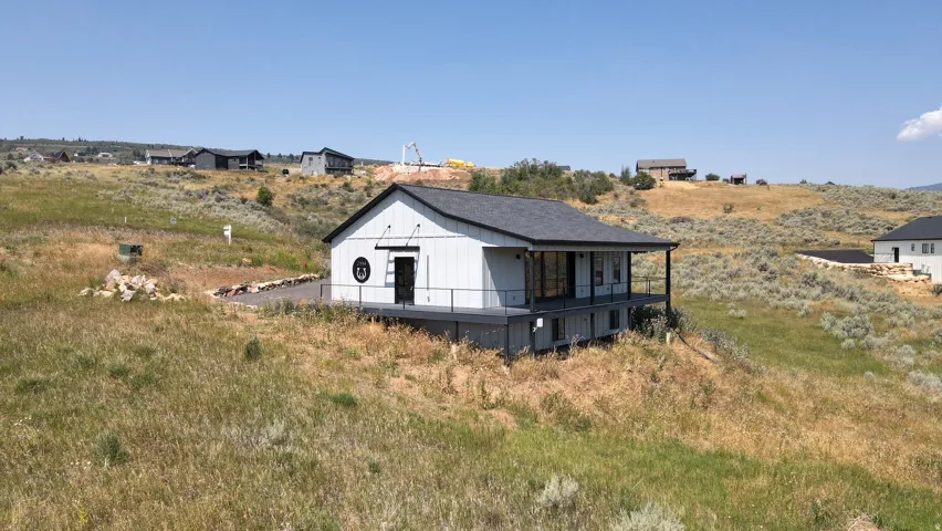 Modern farmhouse style residence featuring a black asphalt shingle roof, white vertical siding, a covered deck with dark railings, and prominent glass doors