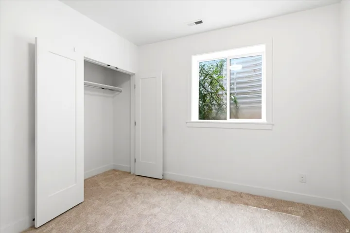 Room featuring neutral-toned carpet, a window with white trim, and a built-in closet with white doors and interior shelving