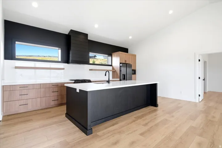 Modern kitchen featuring a black accent wall, light wood-finish flooring, and a vaulted ceiling