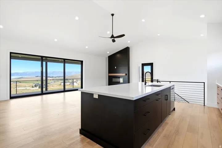 Open-concept living area featuring light wood-finish flooring, a contemporary kitchen island with a white countertop and dark cabinetry, and expansive sliding glass doors