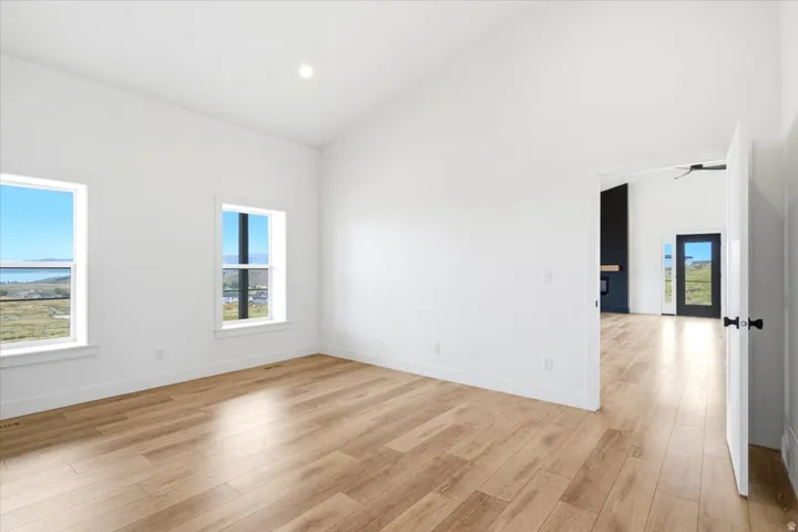 Spacious room featuring vaulted ceilings, recessed lighting, wood-finish flooring, and two windows showcasing a distant body of water and mountains