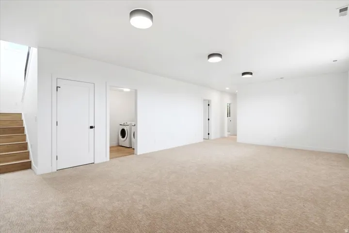 Expansive carpeted area with neutral-toned walls, recessed lighting, and a visible laundry area featuring a washer and dryer