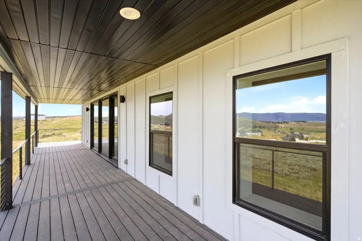 Expansive covered outdoor deck featuring dark wood-finish flooring, recessed lighting, black metal railings, and a white board-and-batten exterior