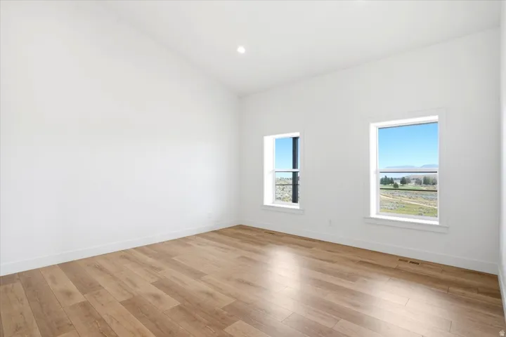 Bright room featuring vaulted ceilings, recessed lighting, wood-finish flooring, and two windows with white trim