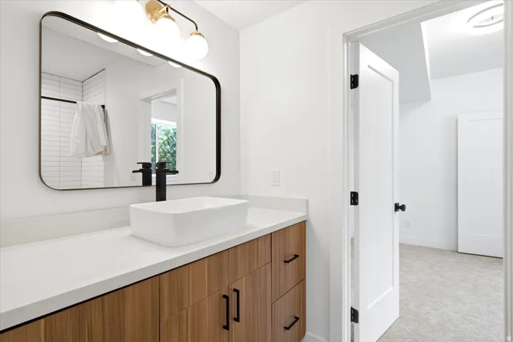 Bathroom featuring a wood-finish vanity with a light-toned countertop, a rectangular vessel sink, and a wall-mounted matte black faucet