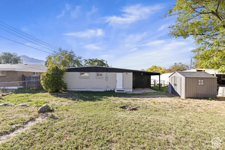 Single-story exterior featuring light-colored siding, a covered patio area, and a detached storage structure set within a fenced yard