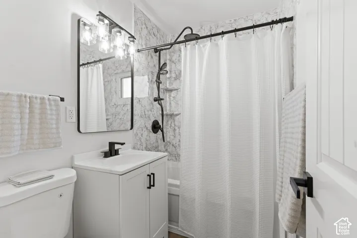 Bathroom featuring a white vanity with a rectangular sink, matte black hardware, patterned tile tub surround, and a coordinating vanity mirror with integrated multi-bulb lighting