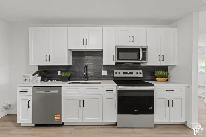 Kitchen featuring white Shaker-style cabinetry, dark tile backsplash, stainless steel appliances, quartz countertops, and matte black hardware