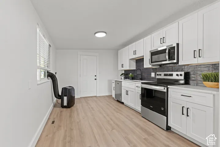 Kitchen featuring white shaker-style cabinetry, wood-finish flooring, stainless steel appliances, and dark horizontal tile backsplash