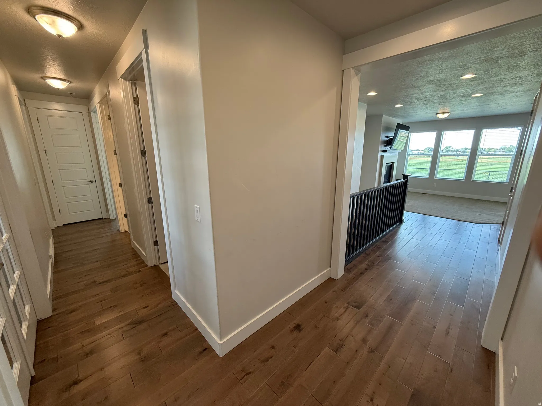 Wood-finish flooring, white trim, and a black open railing accent the hallway