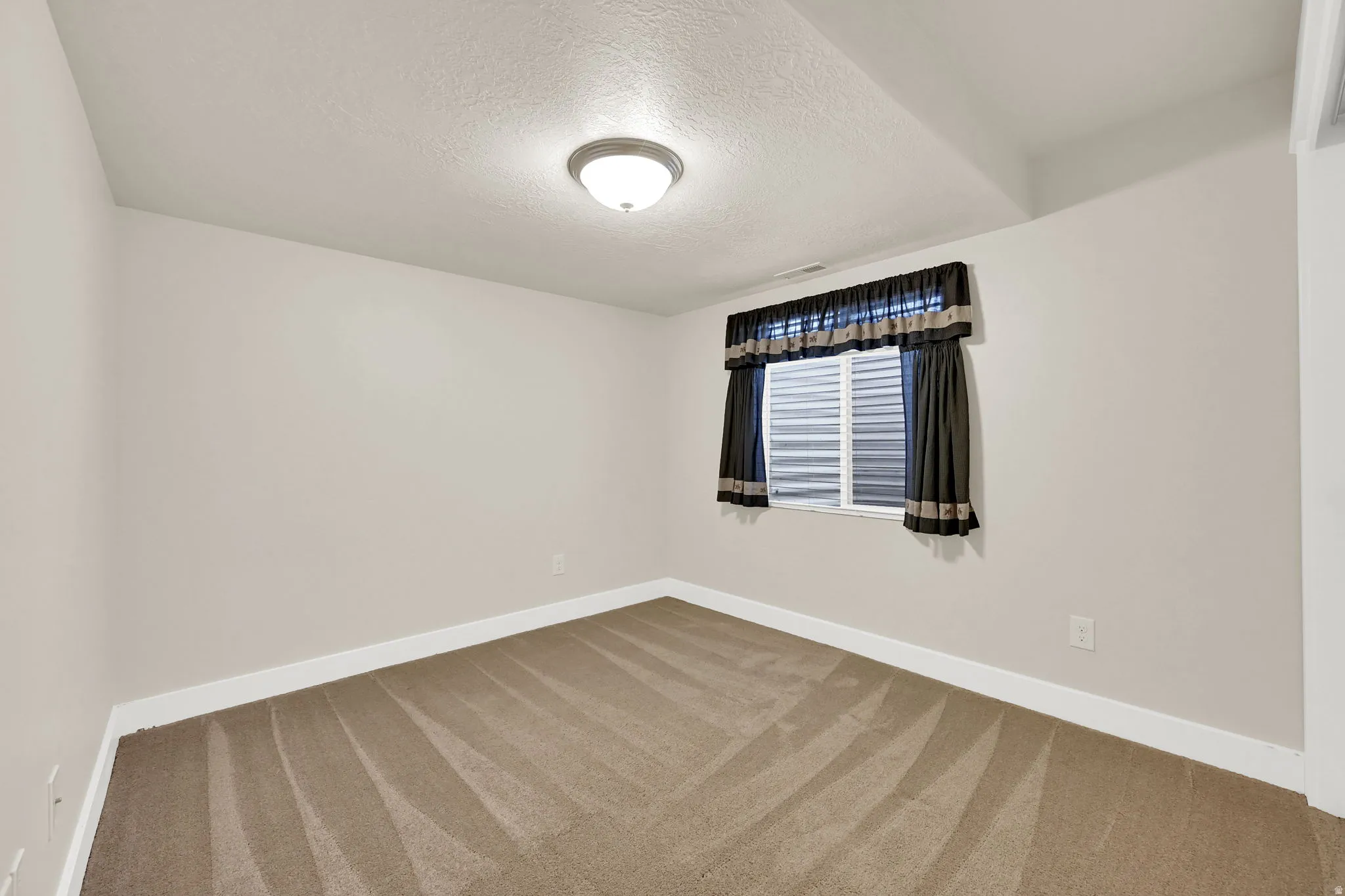 Carpeted room featuring a white-framed window with horizontal blinds, neutral wall paint, and white baseboards