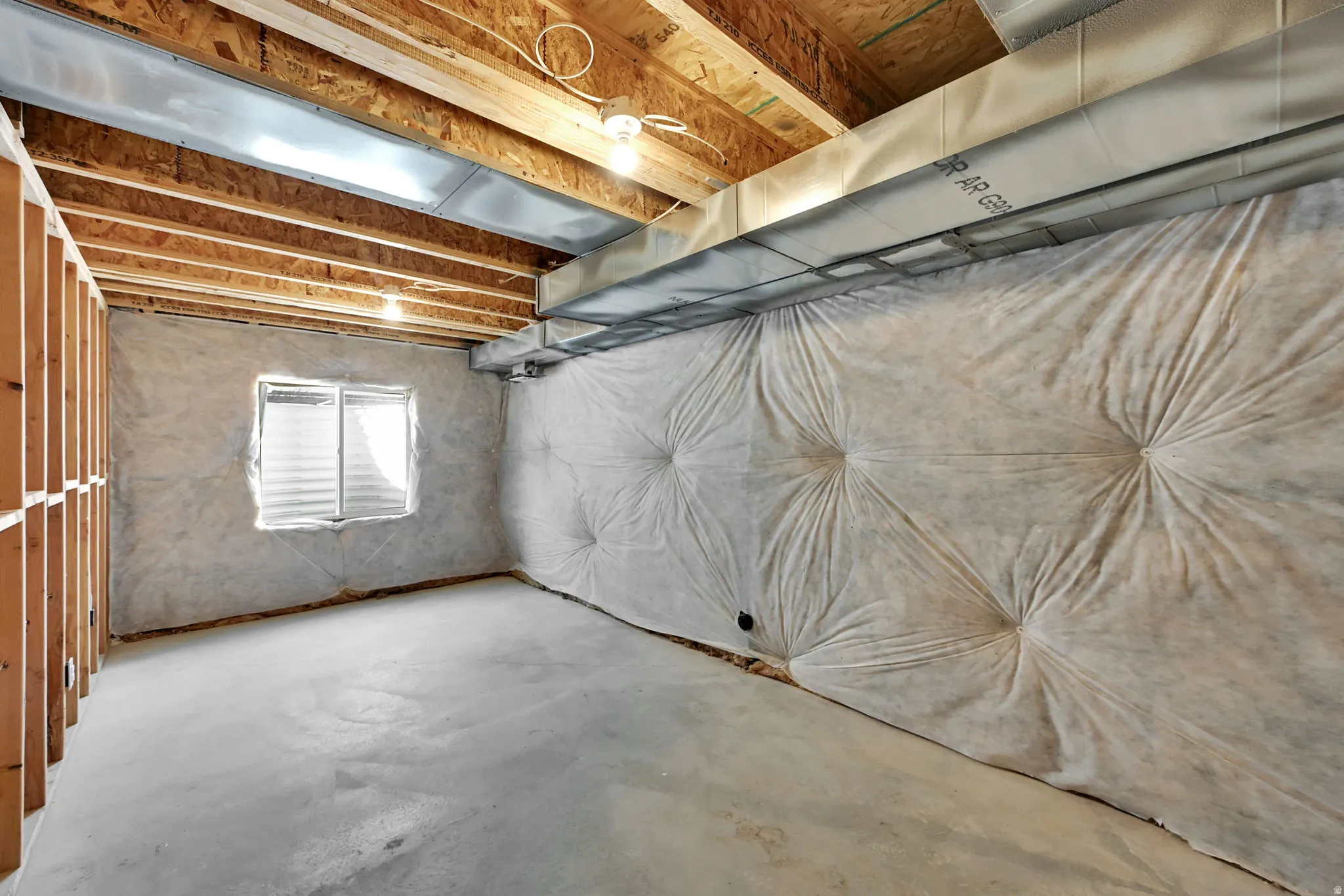 Unfinished lower level featuring exposed ceiling joists, concrete flooring, perimeter insulation, a single window, and visible HVAC ductwork