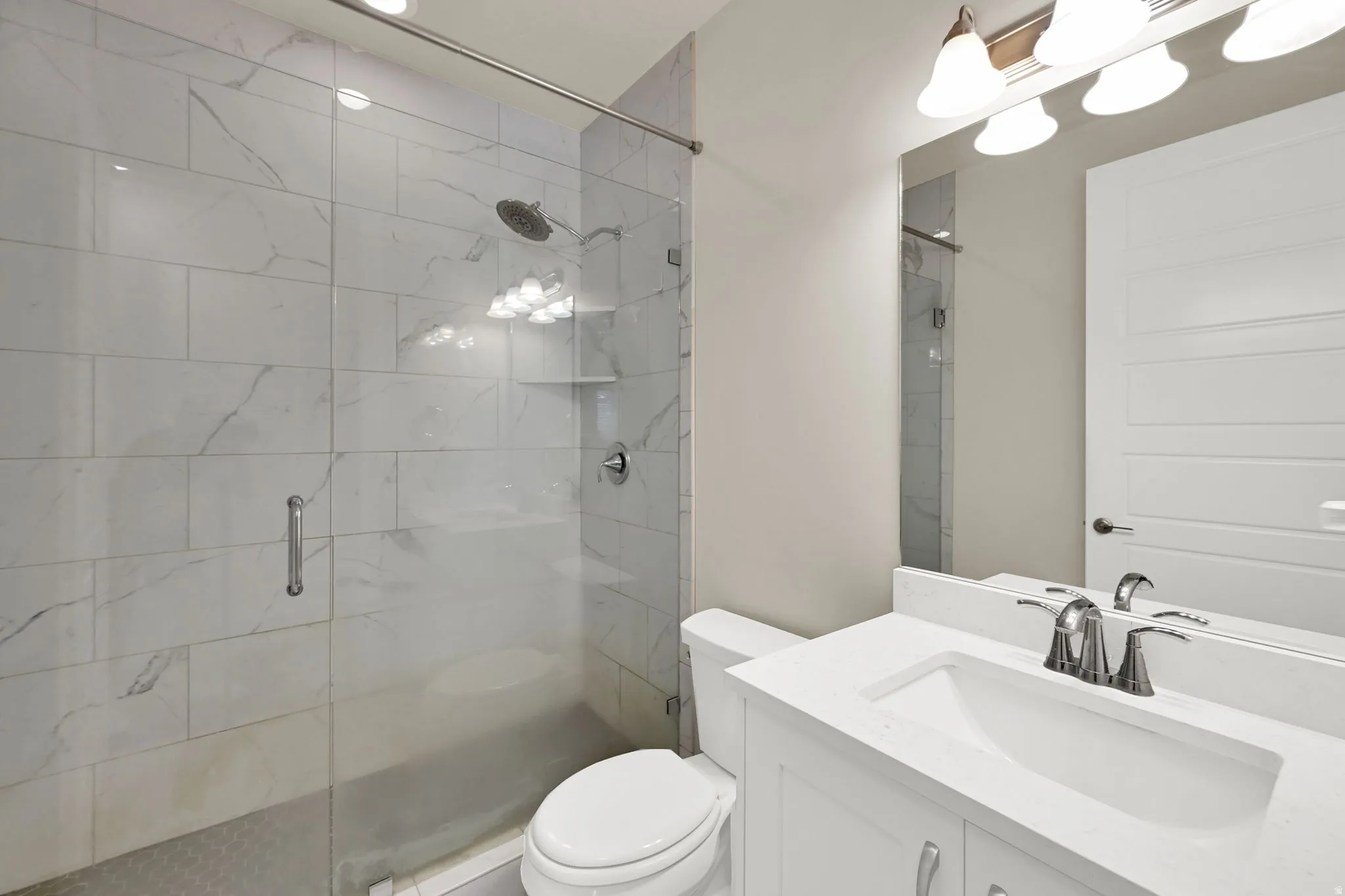 Bathroom featuring a glass-enclosed shower with large format tile surround, a built-in shower shelf, and a rainfall showerhead