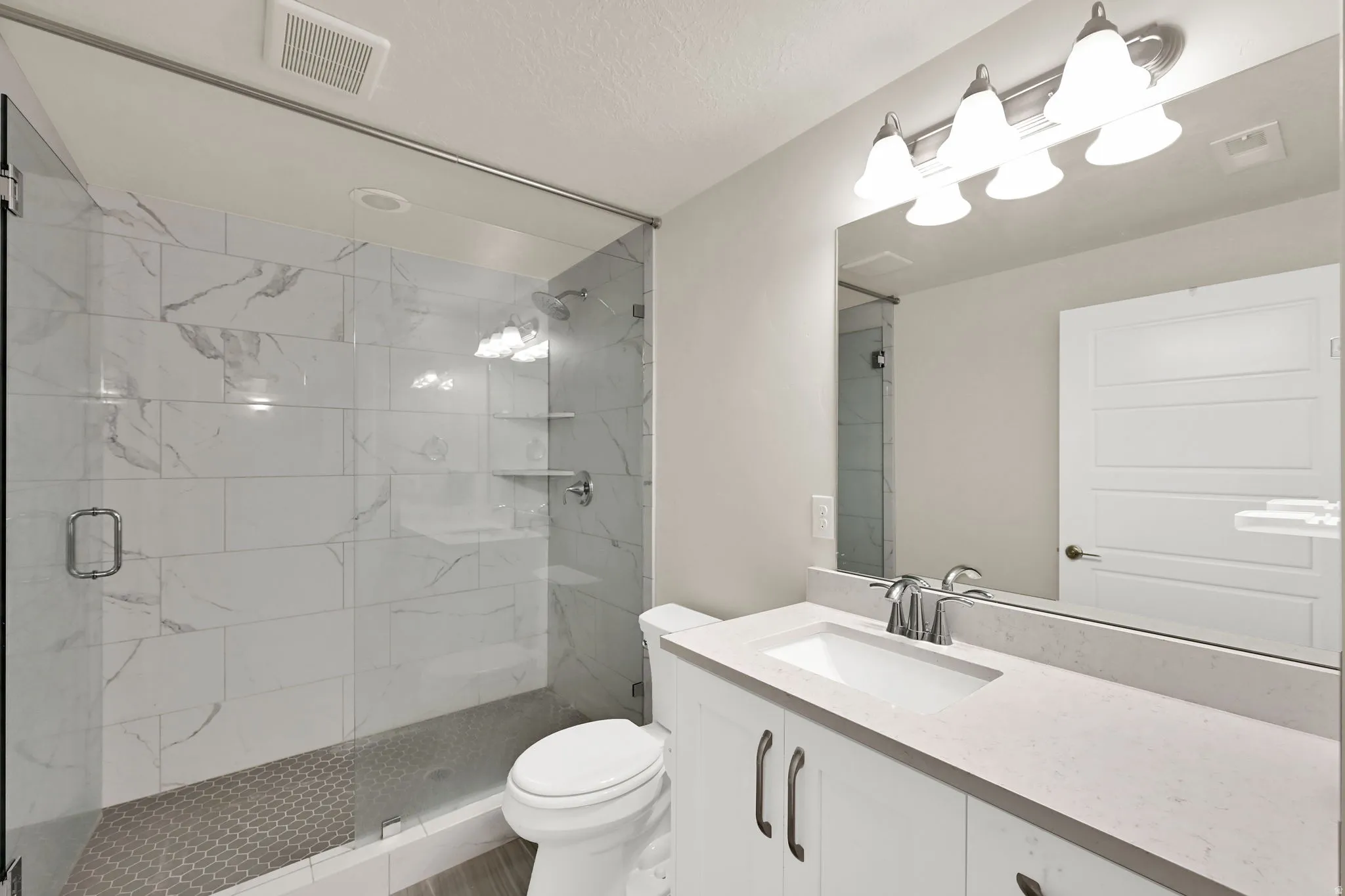Bathroom featuring a frameless glass shower enclosure with white marble-look subway tile and a hexagonal tile shower floor