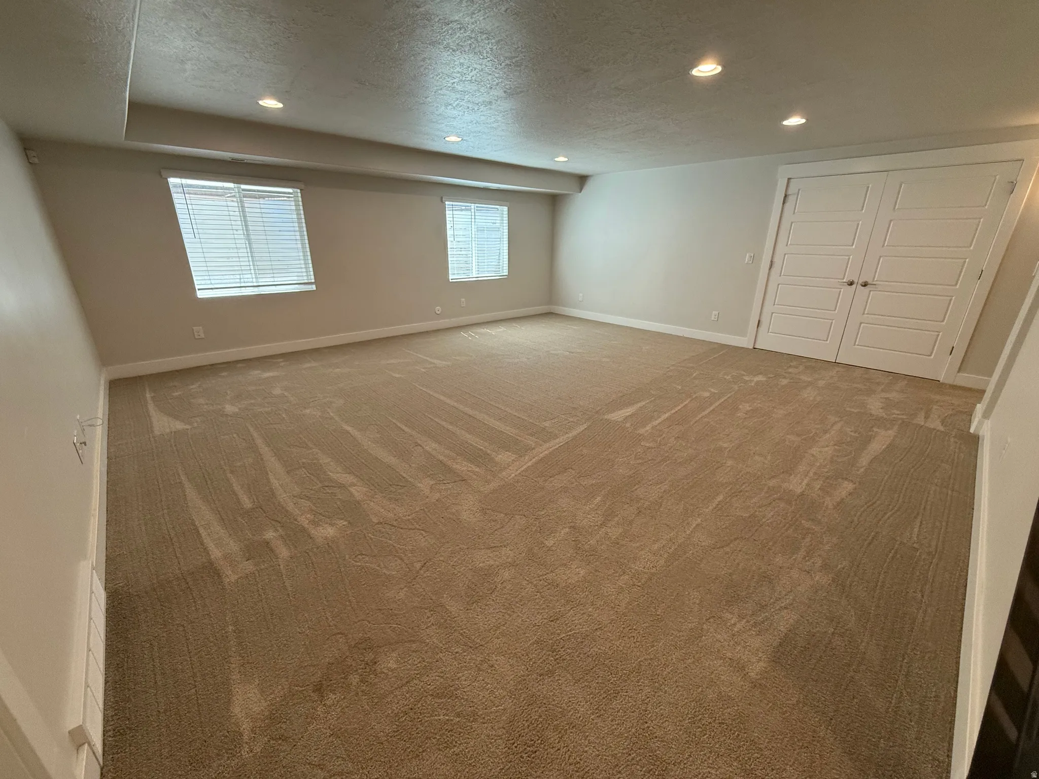 Spacious room featuring neutral carpeting, recessed ceiling lighting, two windows with blinds, and white paneled doors