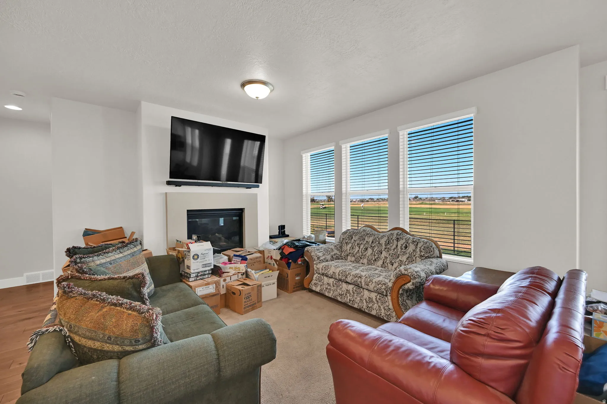Living area featuring multiple windows with blinds, a fireplace with a light-toned surround, a wall-mounted television, and overhead lighting