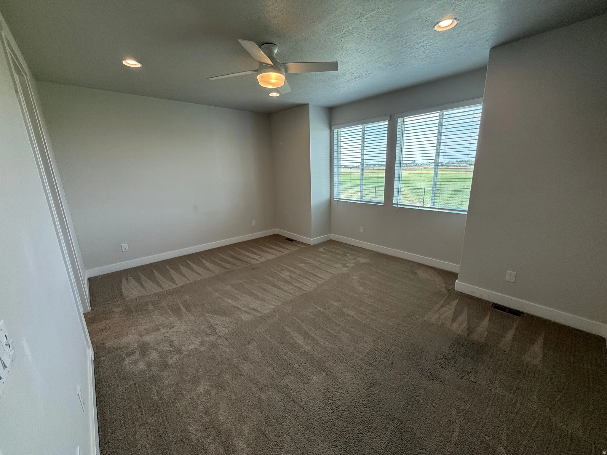 Recessed lighting, ceiling fan, two windows with horizontal blinds, neutral carpet, and light-toned walls