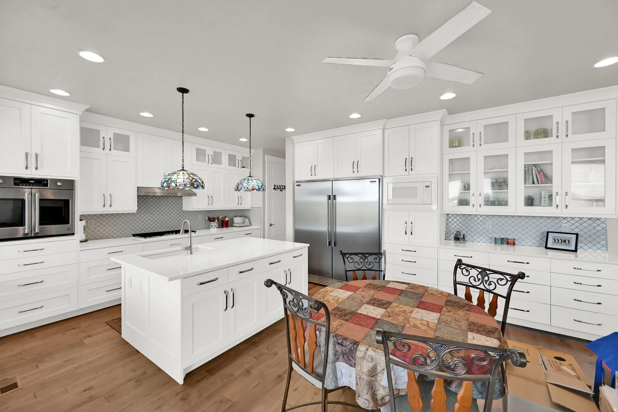 Kitchen featuring an expansive center island with an undermount sink, white shaker cabinetry with brushed nickel hardware, stainless steel appliances, a tile backsplash, and wood-finish flooring
