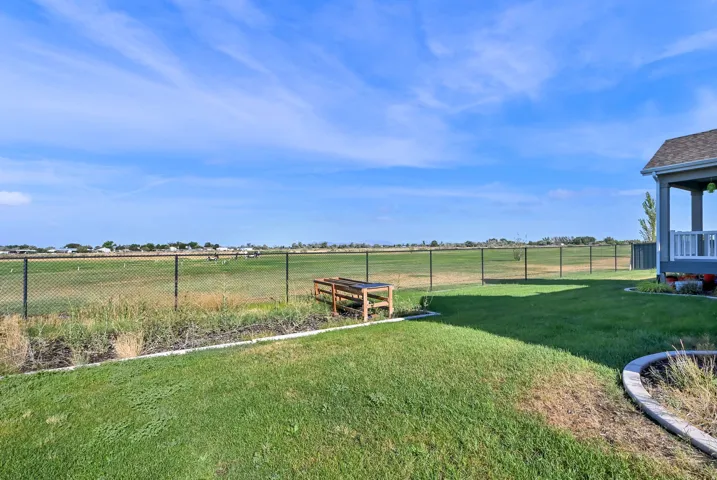 Expansive backyard featuring a green lawn, mature landscaping, a covered patio with white railing, and a black chain link fence