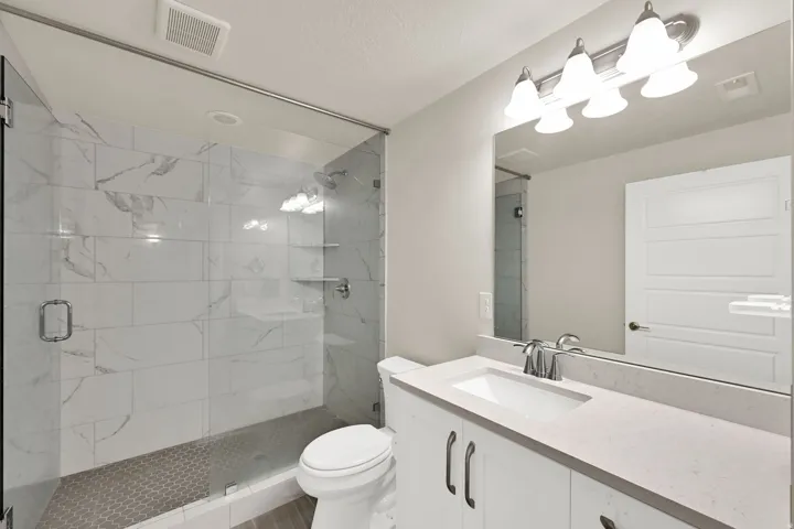 Bathroom featuring a frameless glass shower enclosure with white marble-look subway tile and a hexagonal tile shower floor