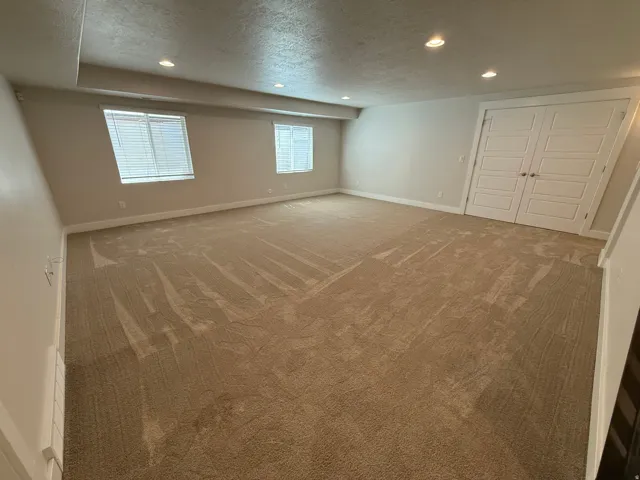 Spacious room featuring neutral carpeting, recessed ceiling lighting, two windows with blinds, and white paneled doors