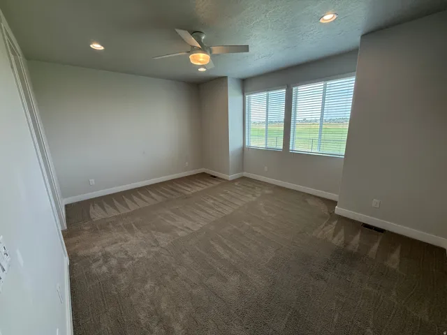Recessed lighting, ceiling fan, two windows with horizontal blinds, neutral carpet, and light-toned walls