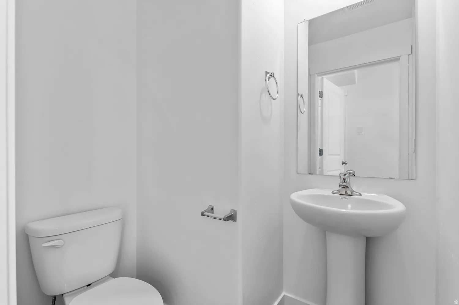 Pedestal sink with chrome faucet, mirror, and white toilet in a brightly lit space