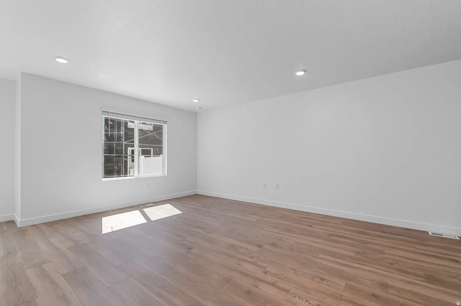 Spacious room featuring wood-finish flooring, white walls, and recessed lighting