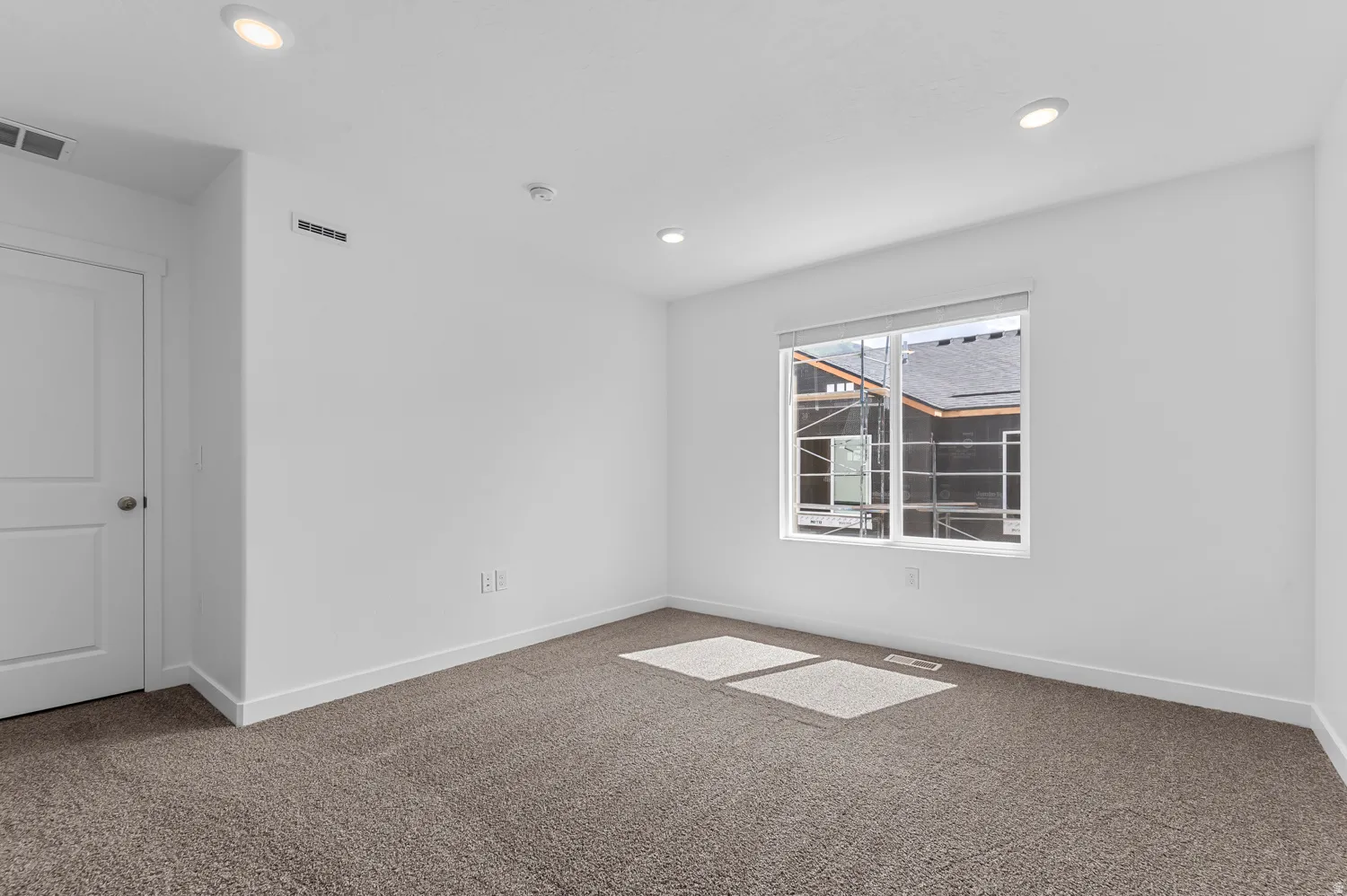 Carpeted room featuring a white interior door, recessed ceiling lighting, a rectangular window with white trim, and white baseboards