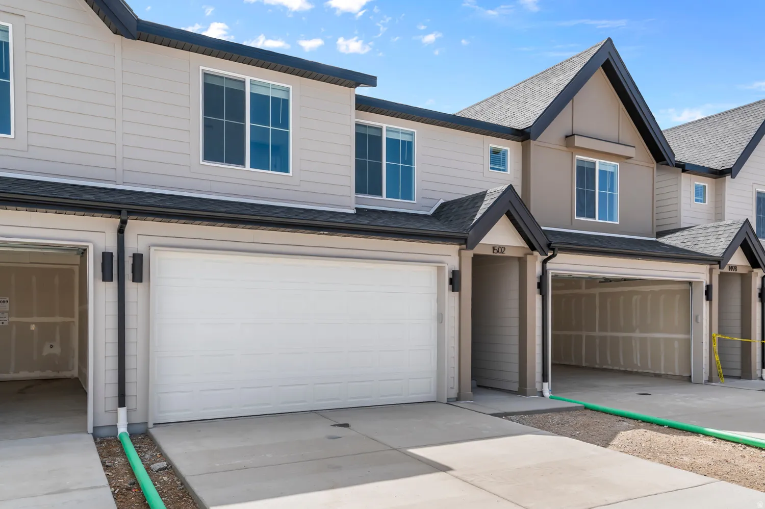 Contemporary townhome community featuring a two-car attached garage with white paneled doors, concrete driveway, and neutral exterior finishes in cream and taupe tones